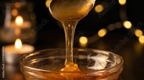 Slow motion honey pouring from spoon into glass bowl