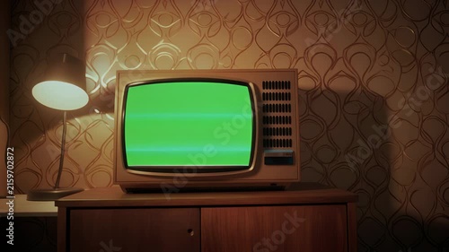 Vintage television with a green screen sits on a wooden cabinet.