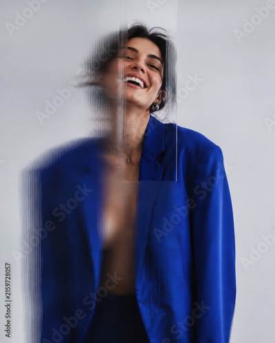 Creative portrait of a joyful woman in a blue blazer behind ribbed glass, with glitch effect and distortion, cinematic fashion photography, blurred and sharp