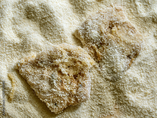 Raw soy cutlet coated in breadcrumbs, placed on a layer of fine breading mixture, prepared for frying.