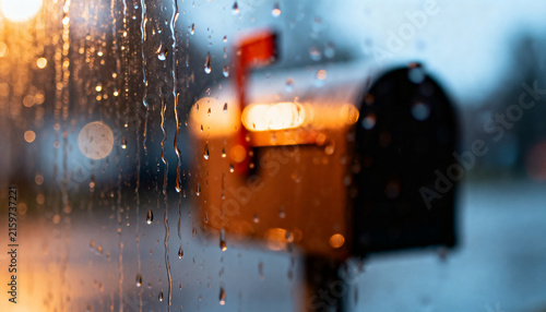 rain drops trickling down a glass surface with a blurry warm mailbox for world post day