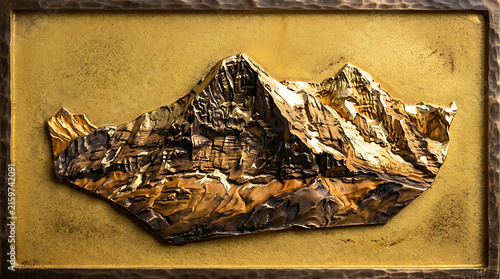 Konstfotografi Mountain Majesty Relief: A textured, golden relief artwork captures the rugged grandeur of a mountain range, showcasing dramatic peaks and shadowed valleys