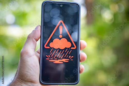 Hand holding smartphone showing rain and flood warning alert icon