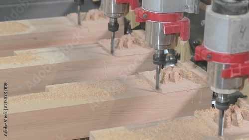 Close-up of a multi-spindle CNC router machine milling intricate carved decorative patterns into wooden workpieces in a furniture manufacturing workshop. Wooden furniture factory and manufacture.