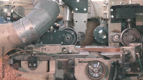 Four-sided woodworking moulder machining a wooden board in an automated production line. Close-up of modern woodworking technology in a furniture factory.