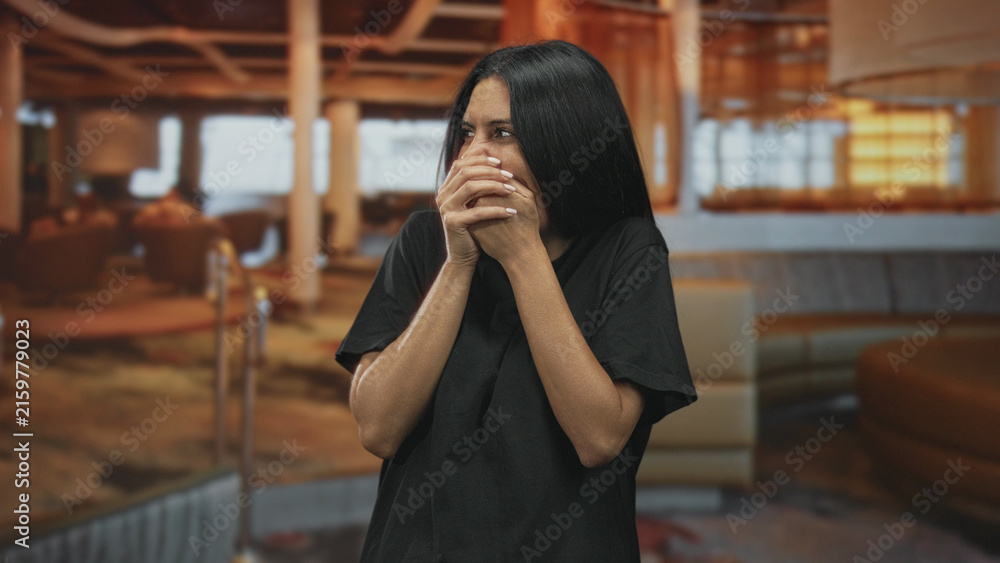 Fototapeta premium Woman covering mouth with hands laughing in airport lounge, shoulders raised and eyes squinting; amusement surprise.