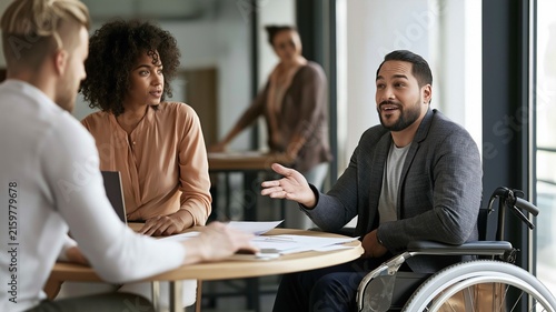 Colleagues in a professional setting, one of whom is in a wheelchair, exchanging ideas