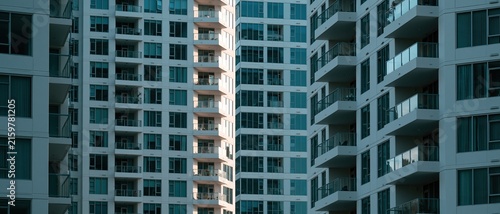 Modern high rise residential apartment building with repetitive grid pattern of glass balconies and blue tinted windows creating a clean cool contemporary city residential facade