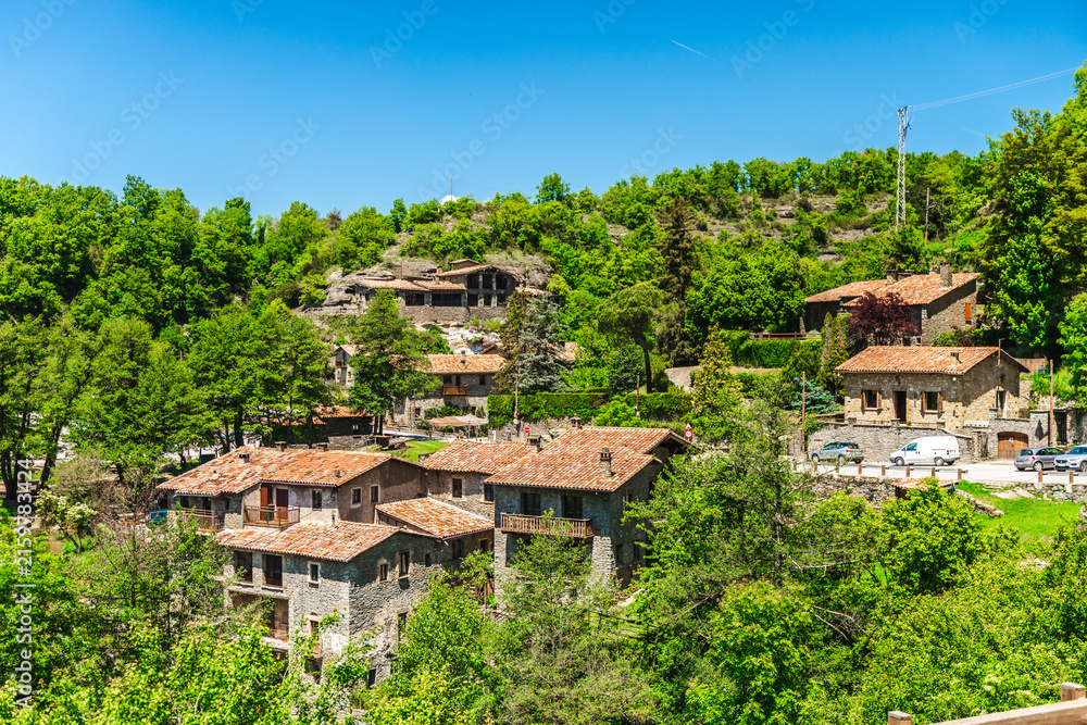 Fototapeta premium Panoramic view of traditional stone houses surrounded by lush green forest in Rupit village, Catalonia, Spain