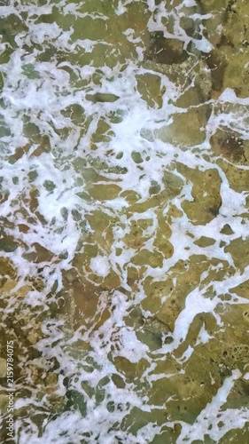 Waves crash against the rocky coastline, their white foam spreading across the rugged shore. The aerial view captures the serene yet powerful dance of the ocean against the earth.