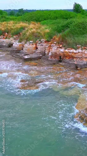 A rugged coastline with waves crashing against rocky outcrops, blending sandy beaches with lush greenery, showcasing the raw beauty of nature along the seaside.