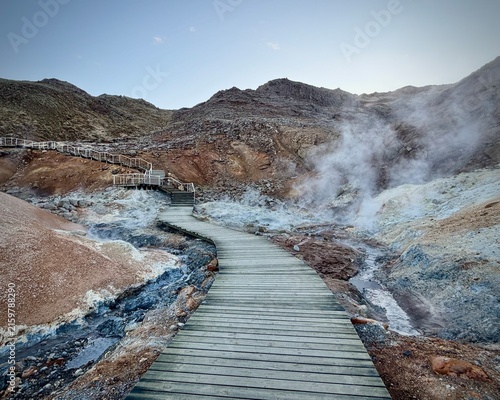 Iceland. Colorful geothermal landscape with steaming blue water and mineral-rich earth, showcasing a series of rocky formations and wooden walkways in a natural hot spring area