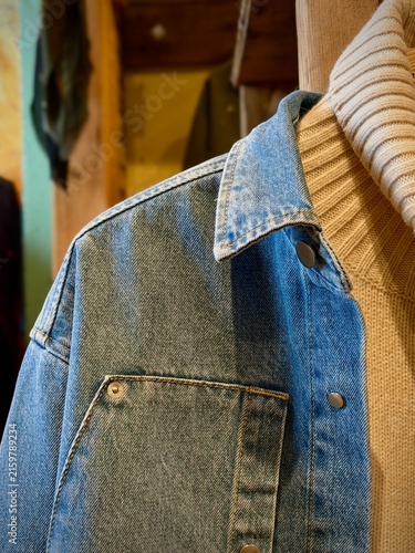 Blaskogabygg, Iceland - May 08, 2026: Denim jackets and sweaters hanging on wooden rack in a clothing store, showcasing various styles and textures for fashion enthusiasts