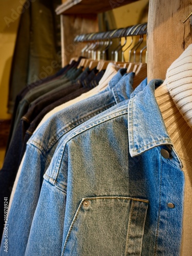 Blaskogabygg, Iceland - May 08, 2026: Denim jackets and sweaters hanging on wooden rack in a clothing store, showcasing various styles and textures for fashion enthusiasts