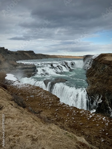 Majestic waterfall Blaskogabygg, Iceland  cascading over rocky cliffs into a turquoise river, surrounded by barren landscape and dramatic clouds in Iceland's natural scenery