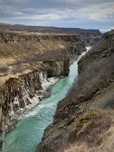 Blaskogabygg, Iceland - May 08, 2026: Scenic view of a winding river flowing through a canyon with steep cliffs and sparse vegetation under a cloudy sky