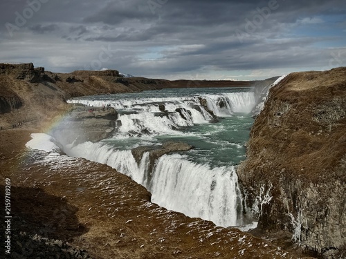 Majestic waterfall Blaskogabygg, Iceland  cascading over rocky cliffs into a turquoise river, surrounded by barren landscape and dramatic clouds in Iceland's natural scenery