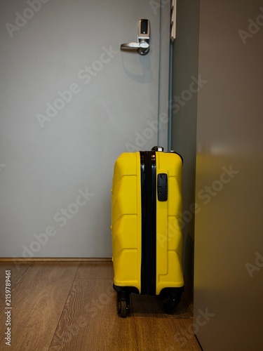 Reykjavik, Iceland - May 09, 2026: Yellow suitcase on wheels stands beside a closed door in a contemporary indoor environment with wooden flooring