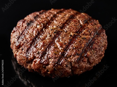 Juicy seasoned beef burger patty with charred grill marks cooking on a hot cast-iron pan