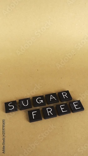 Black square letter tiles spelling out the words sugar free moving on a light brown paper background, representing a healthy diet and lifestyle choice for weight loss and well being