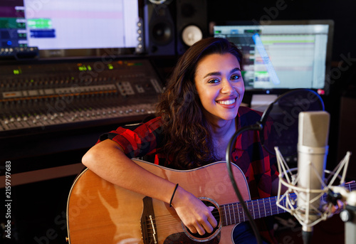 Portrait of a smiling woman guitarist in recording studio looking at camera