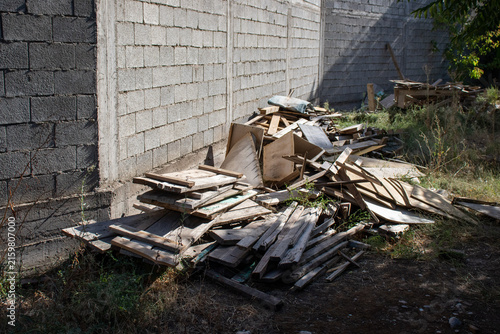 A pile of scrap wood and construction debris dumped near a cinder block wall outdoors. Concept of renovation waste, building site cleanup, and waste management.