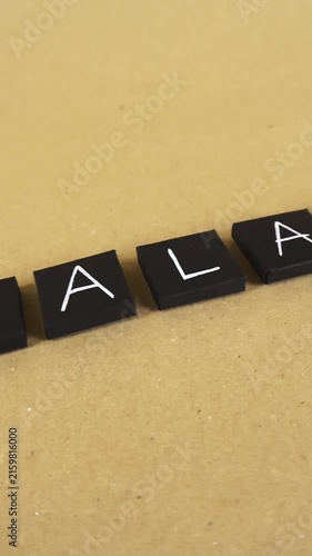 Smooth camera movement over black squares with white letters spelling out the word halal, representing Islamic dietary law and permissible food products on a simple brown cardboard background