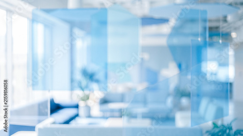 Unfocused bright corporate workspace interior seen through hanging translucent blue acrylic divider panels creating completely blurred abstract background image without recognizable subjects