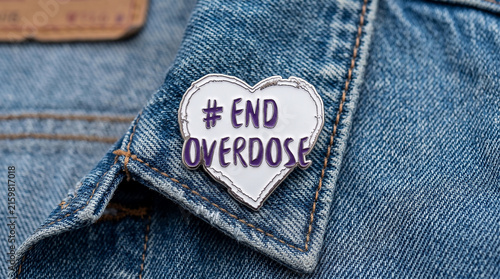 Heart shaped pin badge with End Overdose sign on blue denim jacket collar for International Overdose Awarness Day campaign and substance abuse prevention