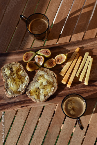 Romantic Mediterranean summer breakfast with figs, cheese and honey served outside with coffee on a wooden board