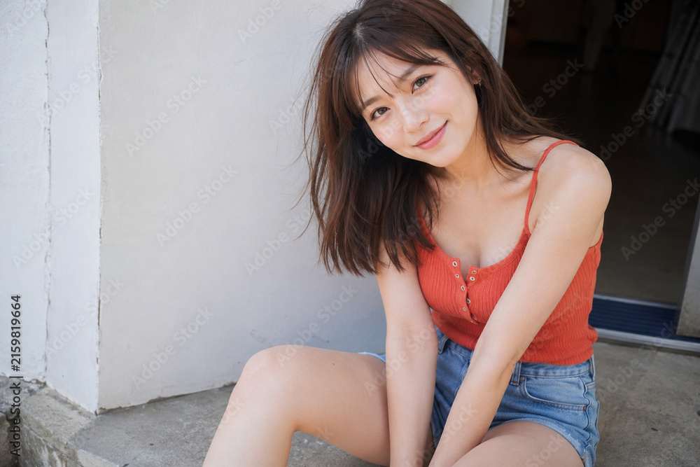 Naklejka premium 赤いタンクトップとデニムショートパンツで玄関前に座る女性