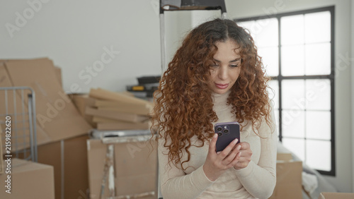 Foto Woman holding smartphone and smiling while surrounded by cardboard boxes and ladder in a building; contentment moving day