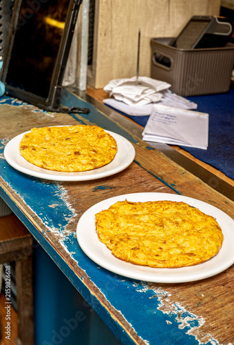 Two individual Spanish omelettes on white plates resting on a rustic wooden bar counter in a local restaurant context.
