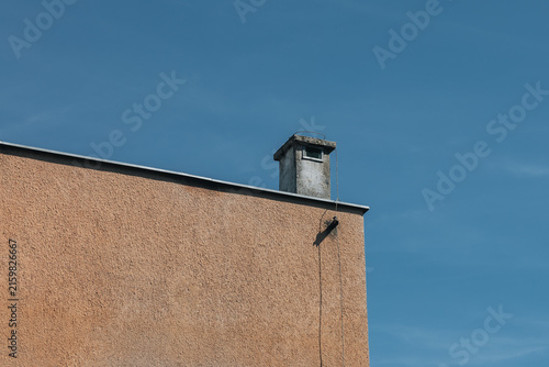 Minimalist building facade with rooftop chimney against blue sky