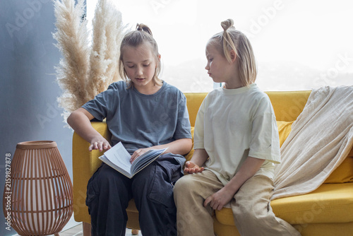Pretty sibling children reads book. Blonde kids with book at home