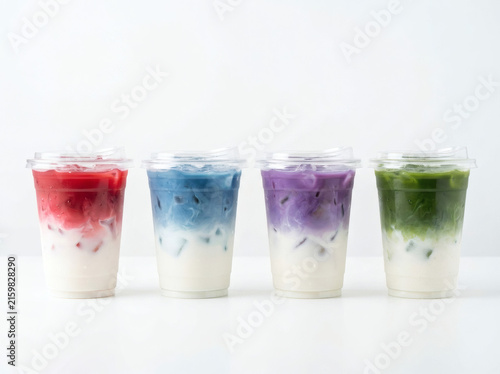 Photograph of four colored matcha latte drinks in clear disposable plastic cups with clear flat plastic lids, arranged in a strict single horizontal line