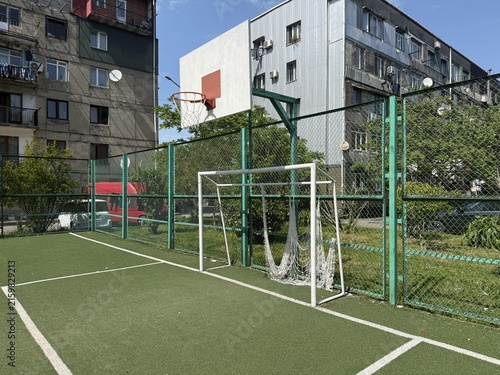 Children play basketball and soccer on an outdoor sports court in a city during a sunny day in summer