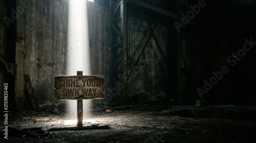 An inspirational wooden sign reading 'Shine Your Own Way' illuminated by a single beam of light in a dark, abandoned industrial warehouse setting.