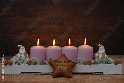 Einen schönen vierten Advent. Rustikales Gesteck dekoriert mit Weihnachtsmann Figuren, Stern und Tannenzweigen vor einem rustikalem Holzhintergrund mit Platz für Text.
