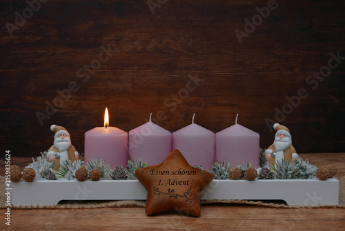 Einen schönen ersten Advent. Rustikales Gesteck dekoriert mit Weihnachtsmann Figuren, Stern und Tannenzweigen vor einem rustikalem Holzhintergrund mit Platz für Text.