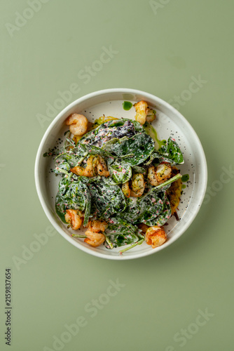 Shrimp salad with greens and dressing served in a bowl on a light table