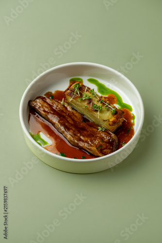 Delicious dish served on a white plate with green sauce and red sauce on a simple background