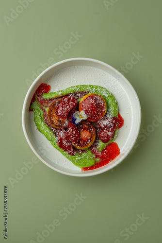 Dessert served on a round plate with green sauce and strawberries on a green background