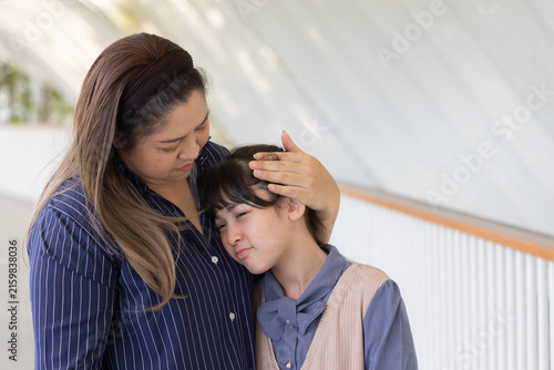 asian middle aged single mother comforting her sad and crying primary school daughter in sunny outdoor scene, motherly love and support