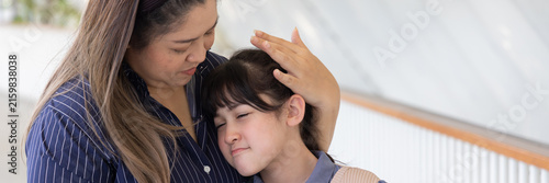 asian middle aged single mother comforting her sad and crying primary school daughter in sunny outdoor scene, motherly love and support