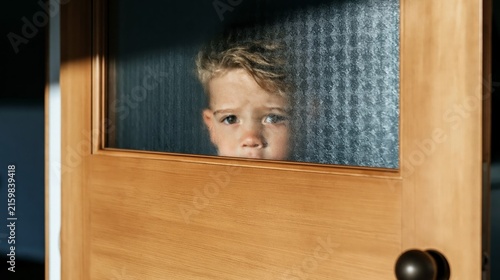 Young child's face visible through frosted glass in a wooden door, showing an expression of apprehension or loneliness