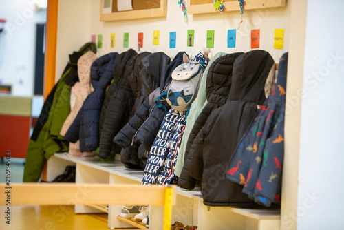 Konstfotografi Le vestiaire d'une école ou d'une garderie avec plusieurs manteaux d'enfants suspendus à des patères au-dessus d'un banc, surmonté d'étiquettes nominatives colorées