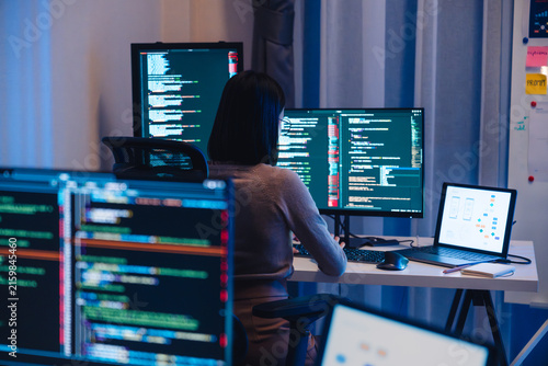 Asian software developers working on multiple screens displaying code and application diagrams at night in modern office