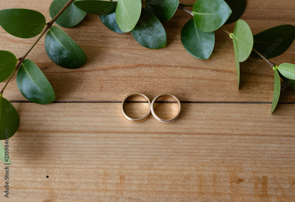 Fototapeta premium Wedding rings and commitment marriage and engagement concept love and partnership golden bands on rustic wooden background with green leaves