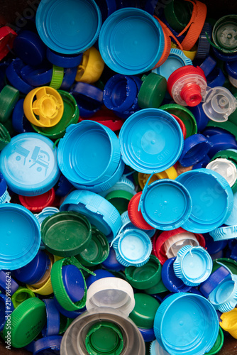 Un grand nombre de bouchons et de couvercles en plastique multicolores (bleus, verts, jaunes, rouges, blancs) rassemblés en vrac, destinés au recyclage ou à des collectes solidaires associatives.